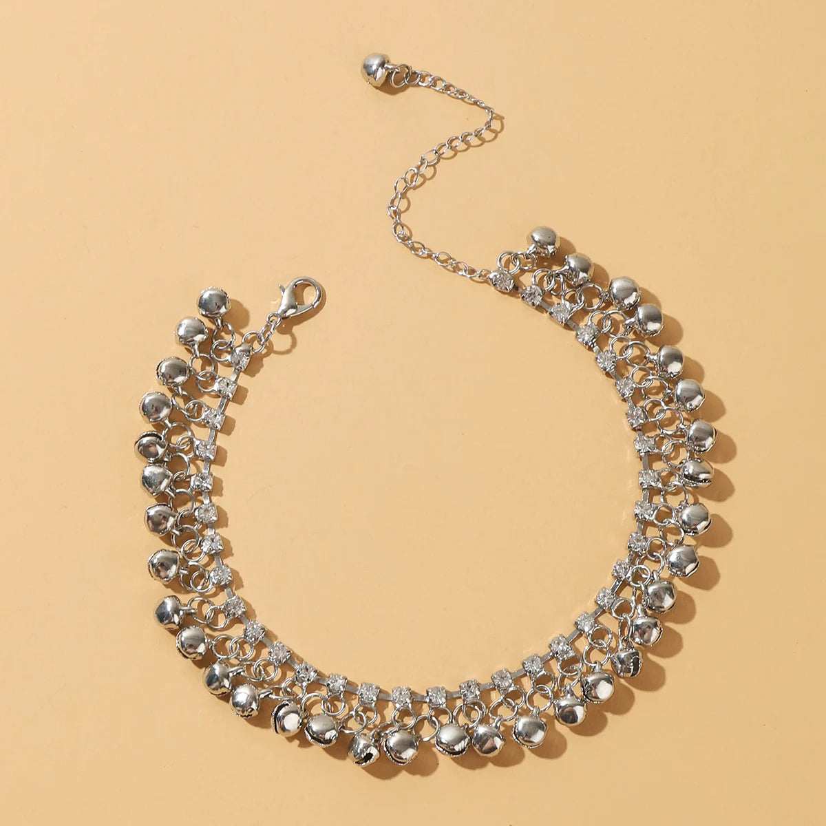 A close-up of an elegant bell foot chain anklet made of silver-toned metal and clear stones.