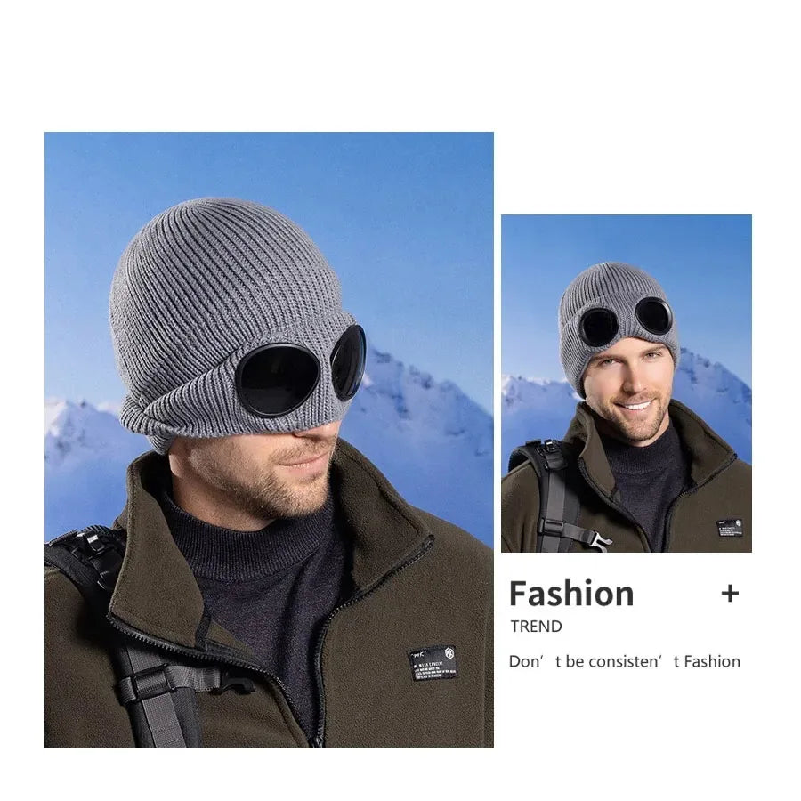 A man wearing a grey knit windproof hat and black sunglasses outdoors.