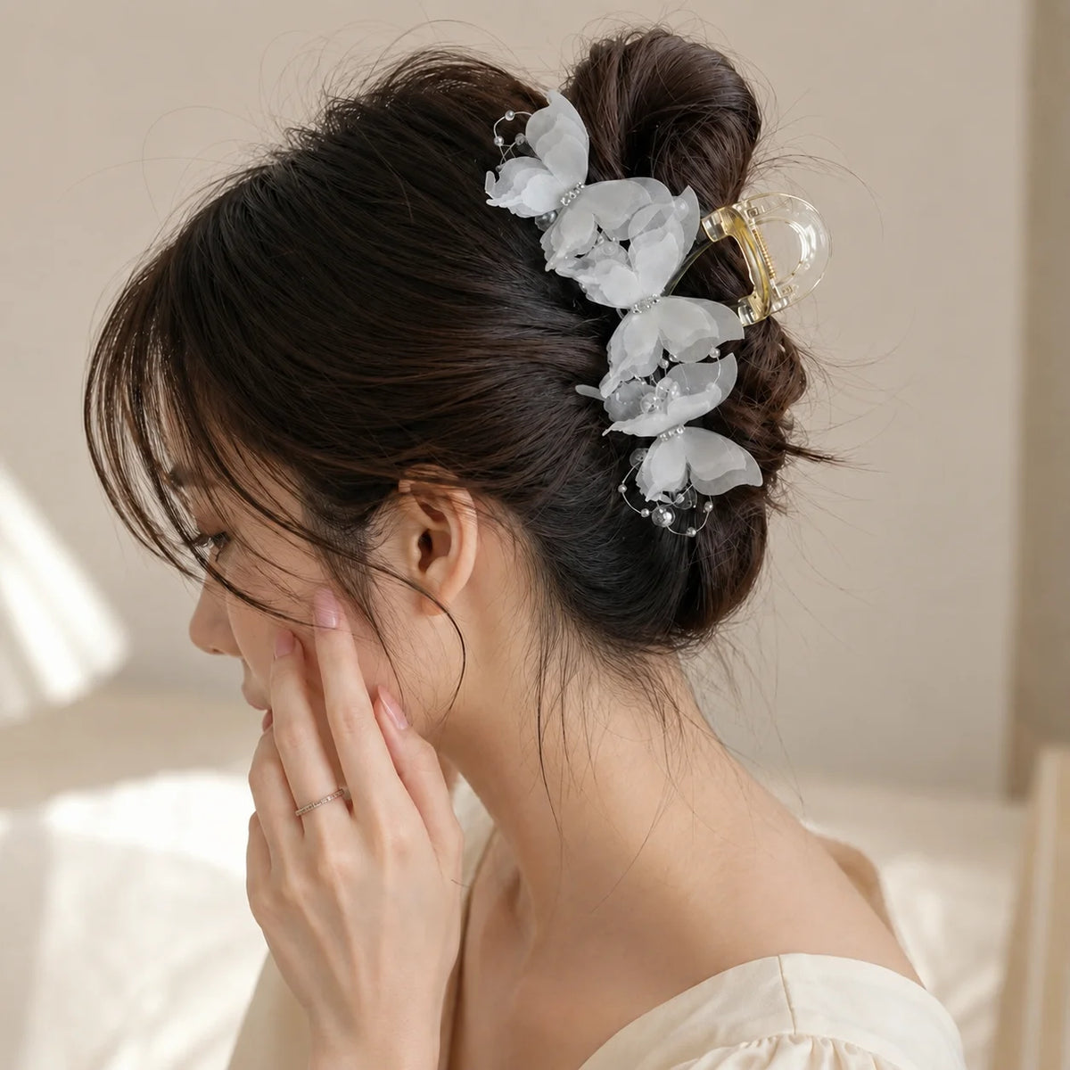 A woman is shown touching her hair while wearing a pearl rhinestone butterfly hair claw clip in an elegant updo.