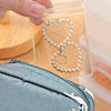 A hand is holding a clear self-sealing jewelry storage pouch containing a gold-toned heart necklace.