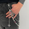 A hand holds a silver pearl cross pendant keychain against dark denim fabric.