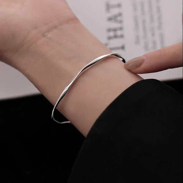 A close-up of a silver twisted wave cuff bracelet worn on a woman's wrist.