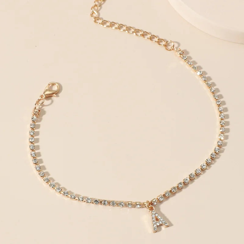 A delicate gold chain anklet bracelet with small clear stones and a letter charm.