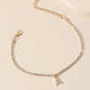 A delicate gold chain anklet bracelet with small clear stones and a letter charm.