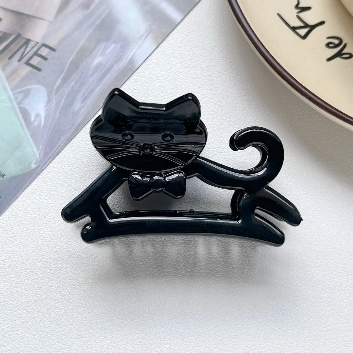 A black cat hair clip featuring a bow, displayed on a white surface.