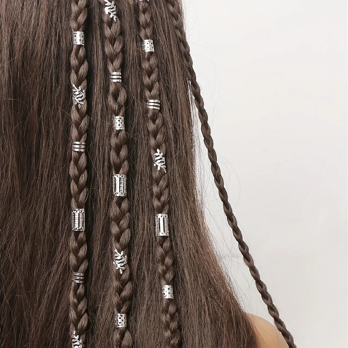 Close-up of dark brown hair featuring multiple braided sections adorned with silver hollow rings