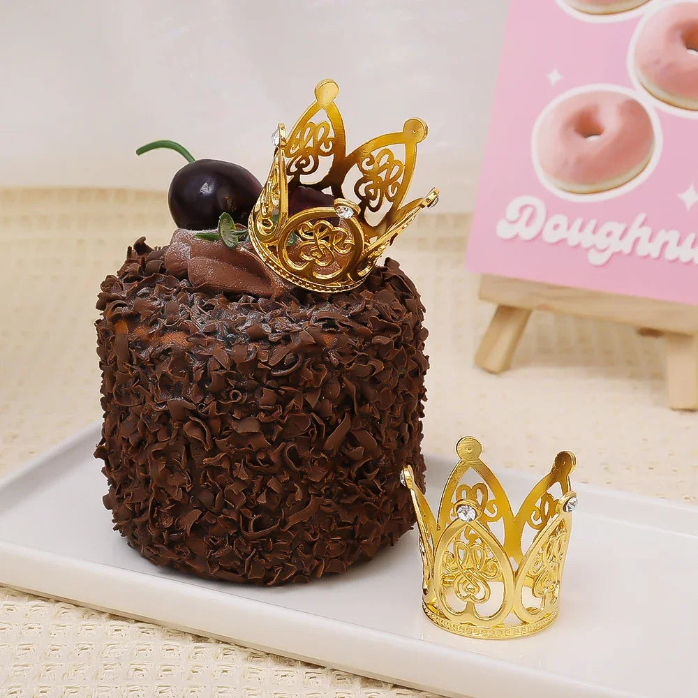 A dark chocolate cake decorated with a gold crown topper and presented on a white plate.