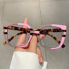 Eine Hand hält eine modische, große, quadratische Brille mit Schildpatt- und rosa Akzenten.