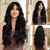 A woman models a long, wavy dark hair wig with long bangs in a brown outfit.