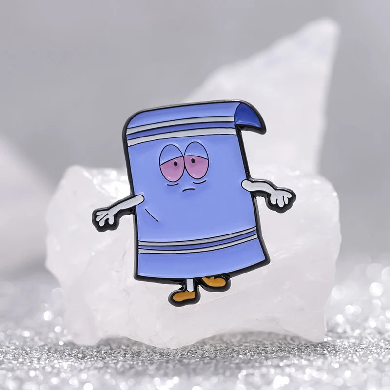 A blue enamel cartoon brooch shaped like a wizard or mage, featuring purple eyes and a striped robe, resting on a white rock.