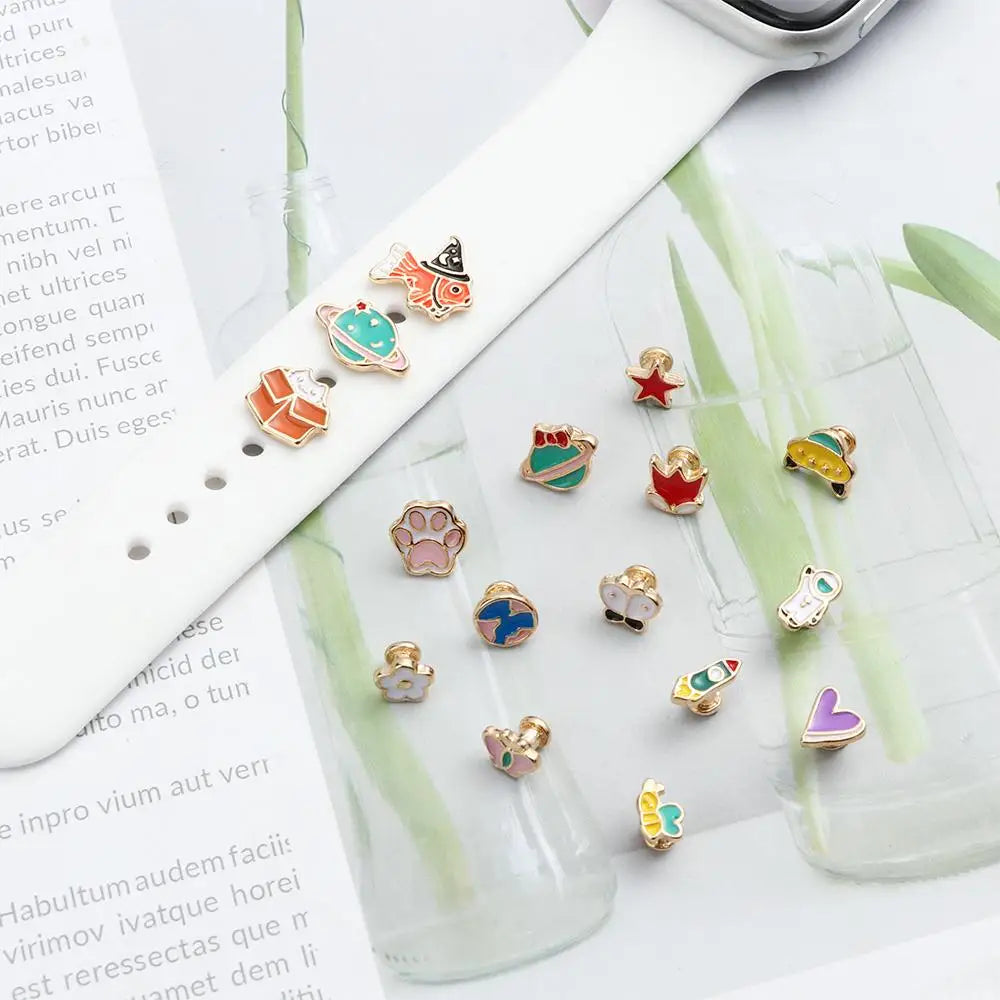 Una pulsera de reloj blanca con adornos metálicos junto a un vaso.