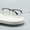 Une paire de lunettes de lecture photochromiques noir et or posée sur une surface blanche.