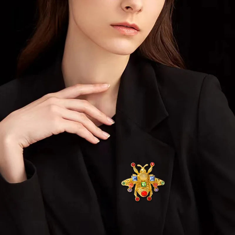 Gros plan d'une femme portant un blazer noir avec une broche de abeille baroque dorée et colorée sur le revers.