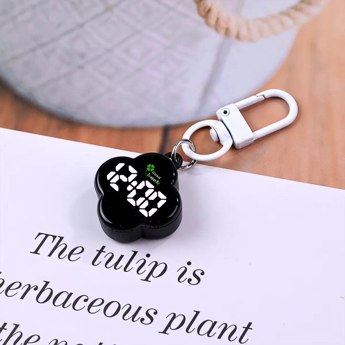 A black LED digital keychain watch with a flower design attached to a white paper.