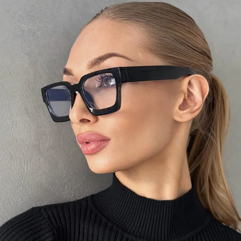 Una mujer vistiendo gafas cuadradas negras vintage contra un fondo gris.