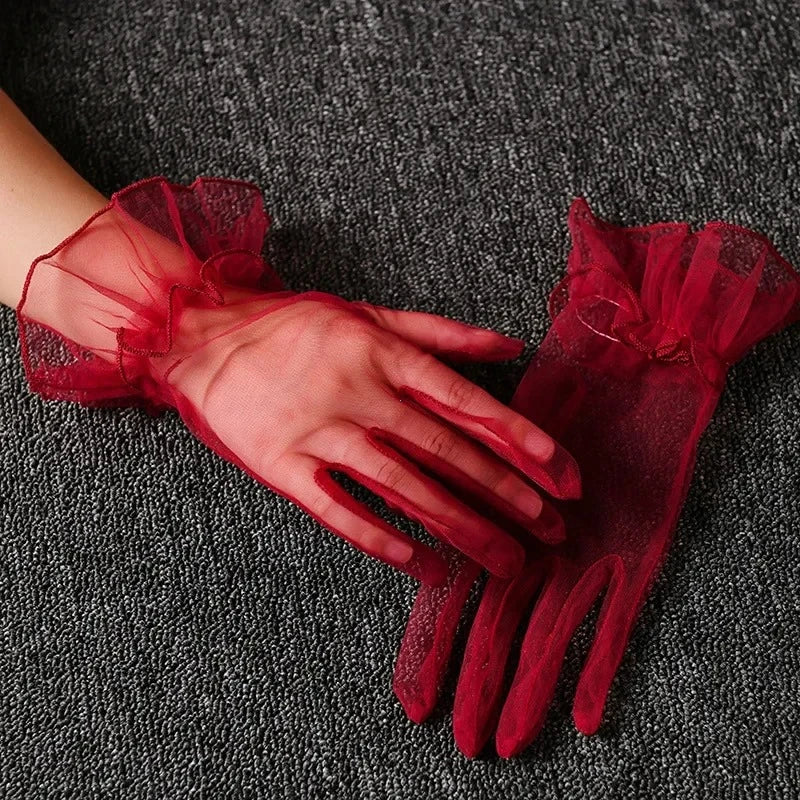 A hand wearing sheer red lace tulle finger gloves resting on a dark gray textured surface.