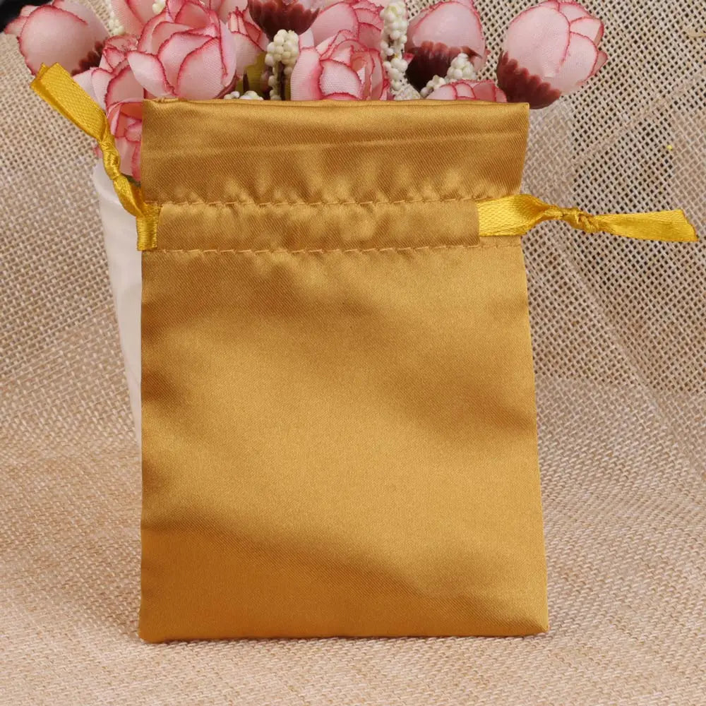 A golden satin drawstring pouch with a yellow tie is displayed next to pink floral decorations.
