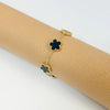 Gold plated stainless steel double-sided petal bracelet with black and gold floral charms on a beige rolled fabric background