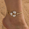Gold-toned bohemian flower pendant anklet worn on a person's ankle against a sandy background.