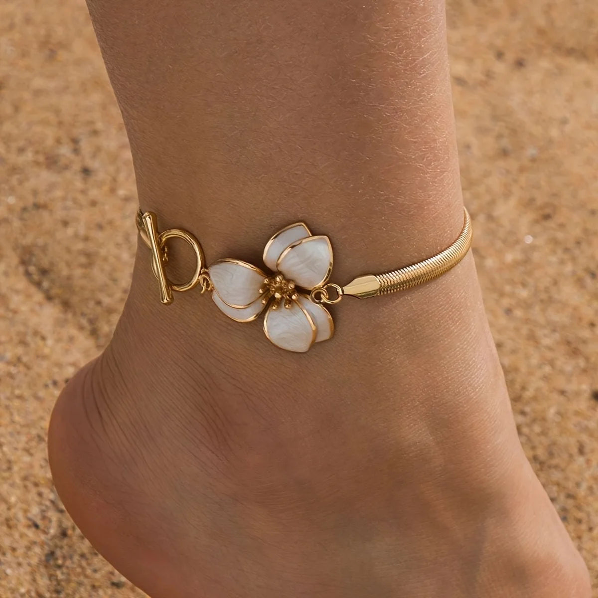 Gold-toned bohemian flower pendant anklet worn on a person's ankle against a sandy background.