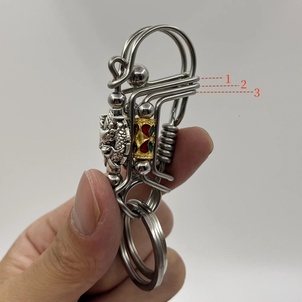 Un porte-clés mécanique en acier inoxydable avec un charm de crâne et un pendentif de couleur or, tenu par une main.