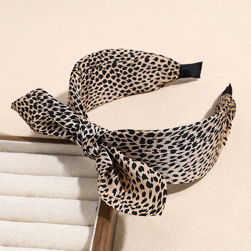 A black and tan leopard print retro bow hairband tied around a head.