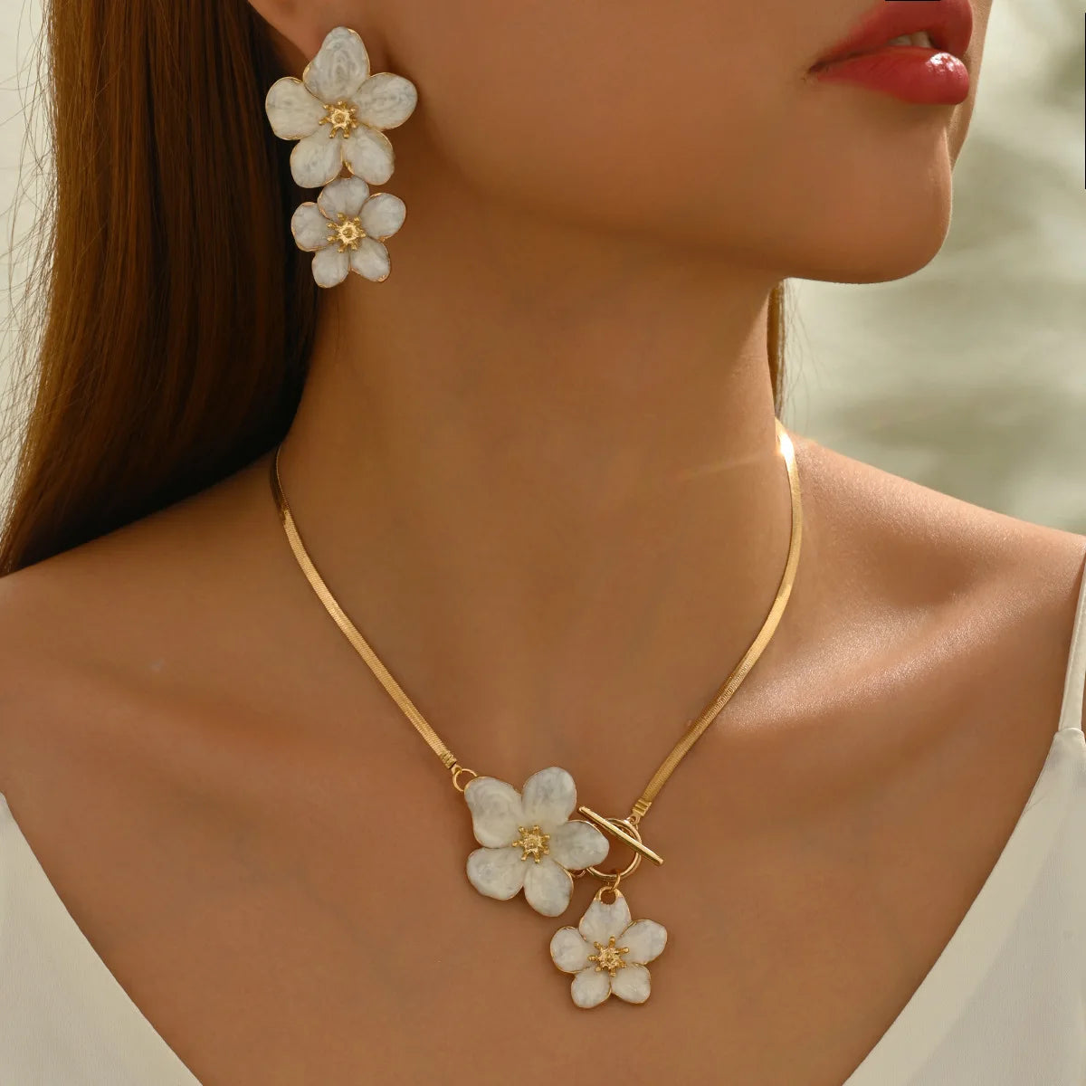 A close-up of a woman wearing a gold floral pendant necklace and matching flower earrings.