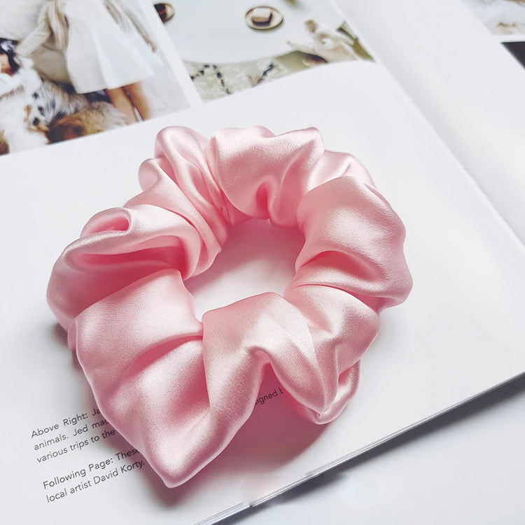 Un lazo de cabello de seda rosa con forma de moño fruncido sobre un cuaderno blanco.