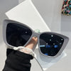 A pair of silver-framed cat eye sunglasses with dark lenses resting on a white surface.