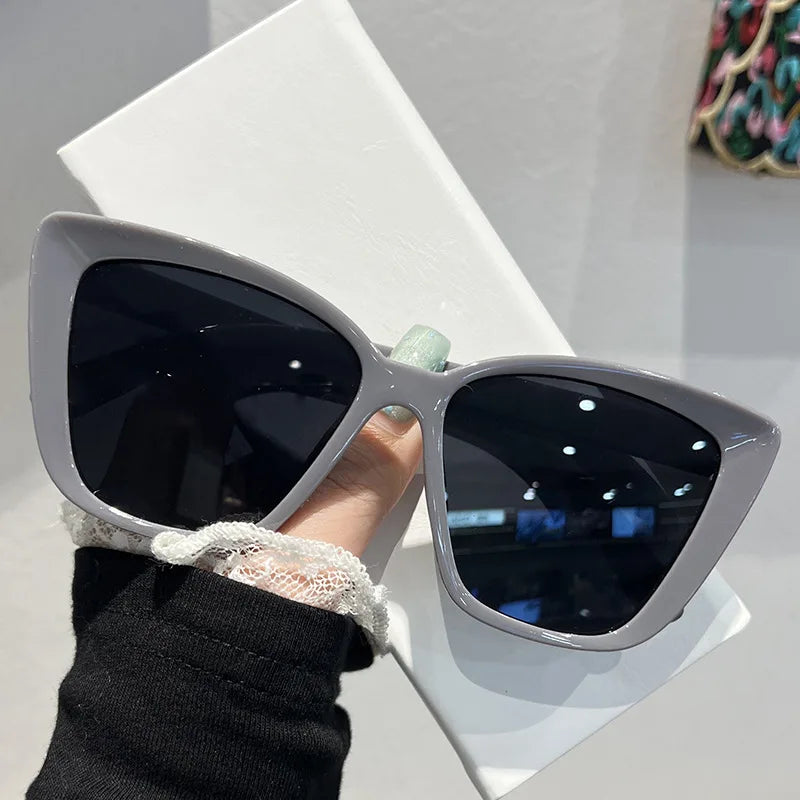 A pair of silver-framed cat eye sunglasses with dark lenses resting on a white surface.