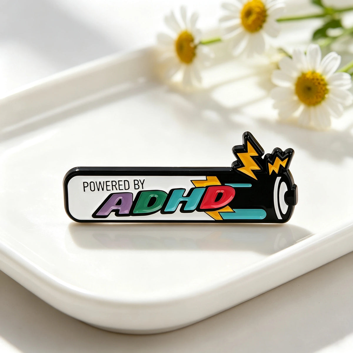 Schwarze Emaille-Anstecknadel mit dem Text ADHD und einem gelben Blitzdesign auf einem weißen Teller.