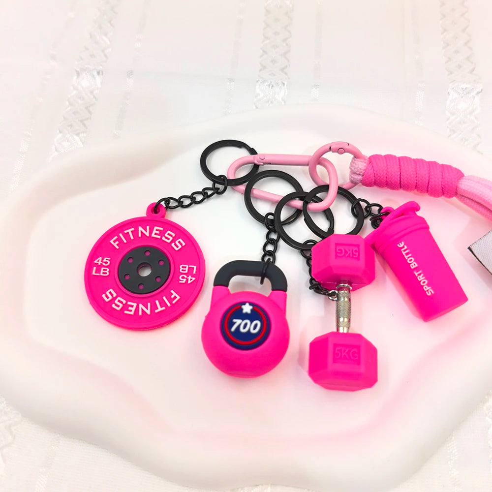 A collection of pink fitness keychains and weightlifting accessories including a 45 lb fitness disc and various sized weights
