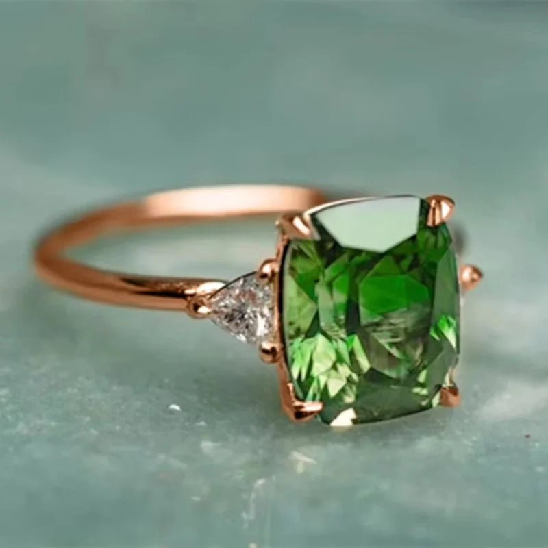 A vintage square gemstone four-claw ring featuring a vibrant green emerald-cut stone set in rose gold.