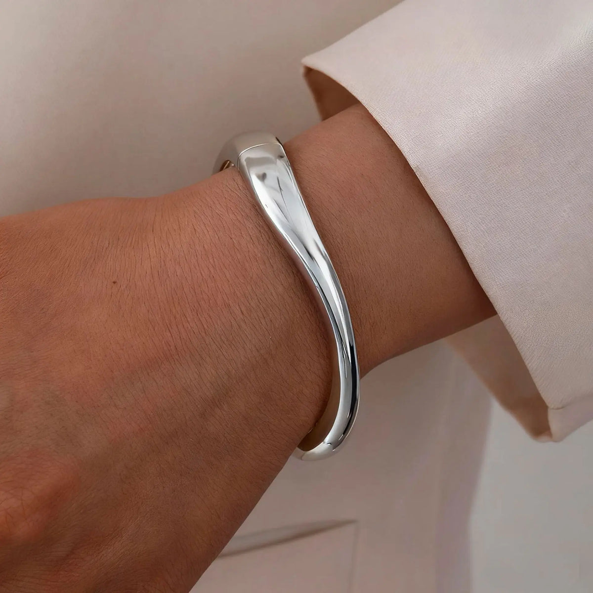 A close-up of a silver cuff bangle bracelet worn on a wrist, next to a light pink sleeve.