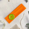Orange fabric hairband with a lime green dot accent on a white background.