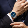 A close-up of a luxury men's quartz watch with a blue luminous dial worn on a wrist, partially visible under a dark suit jack