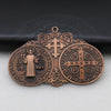 A bronze Saint Benedict protection medal featuring a cross and religious symbols, displayed on a dark surface.