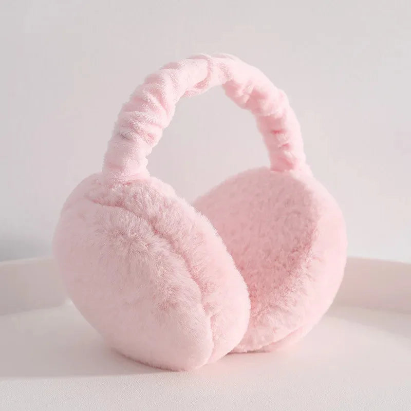 A soft pink plush fur ear warmer or earmuffs resting on a white surface.