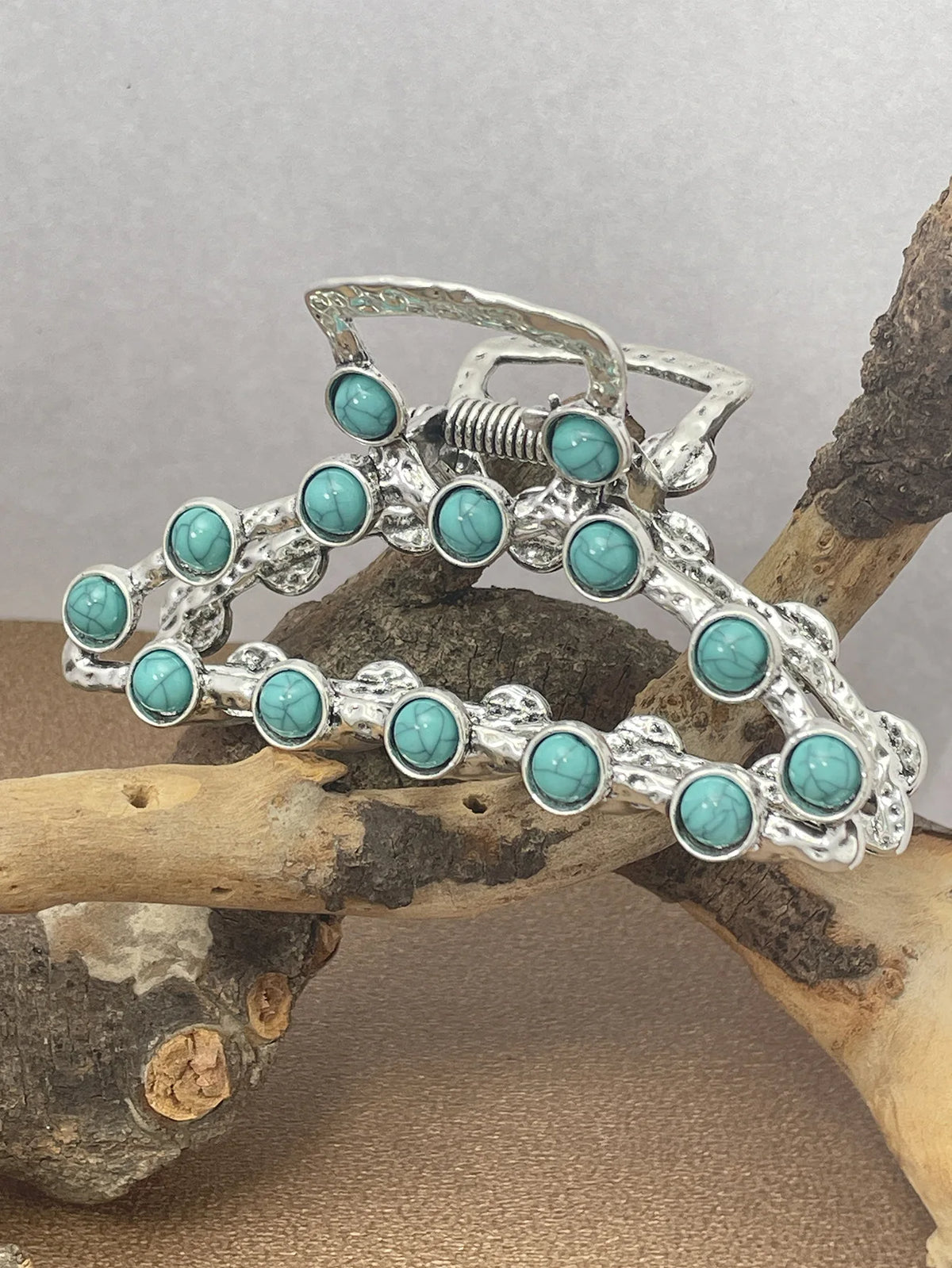 Silver metal hair claw clips decorated with turquoise beads resting on a natural wood branch.
