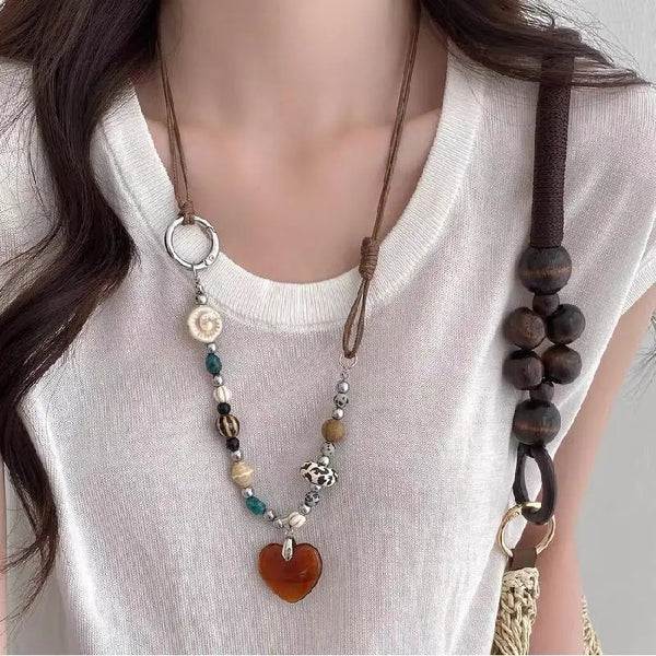 A close-up of a bohemian heart beaded pendant necklace worn against a white t-shirt.