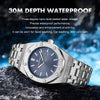 A silver-toned men's watch with a blue dial and metal band resting on a dark rock.