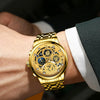 A close-up shot of a gold-toned stainless steel quartz wristwatch with a luminous dial worn on a person's wrist.