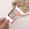 A hand holds a stainless steel tool with a square opening, revealing colorful beads for jewelry making.