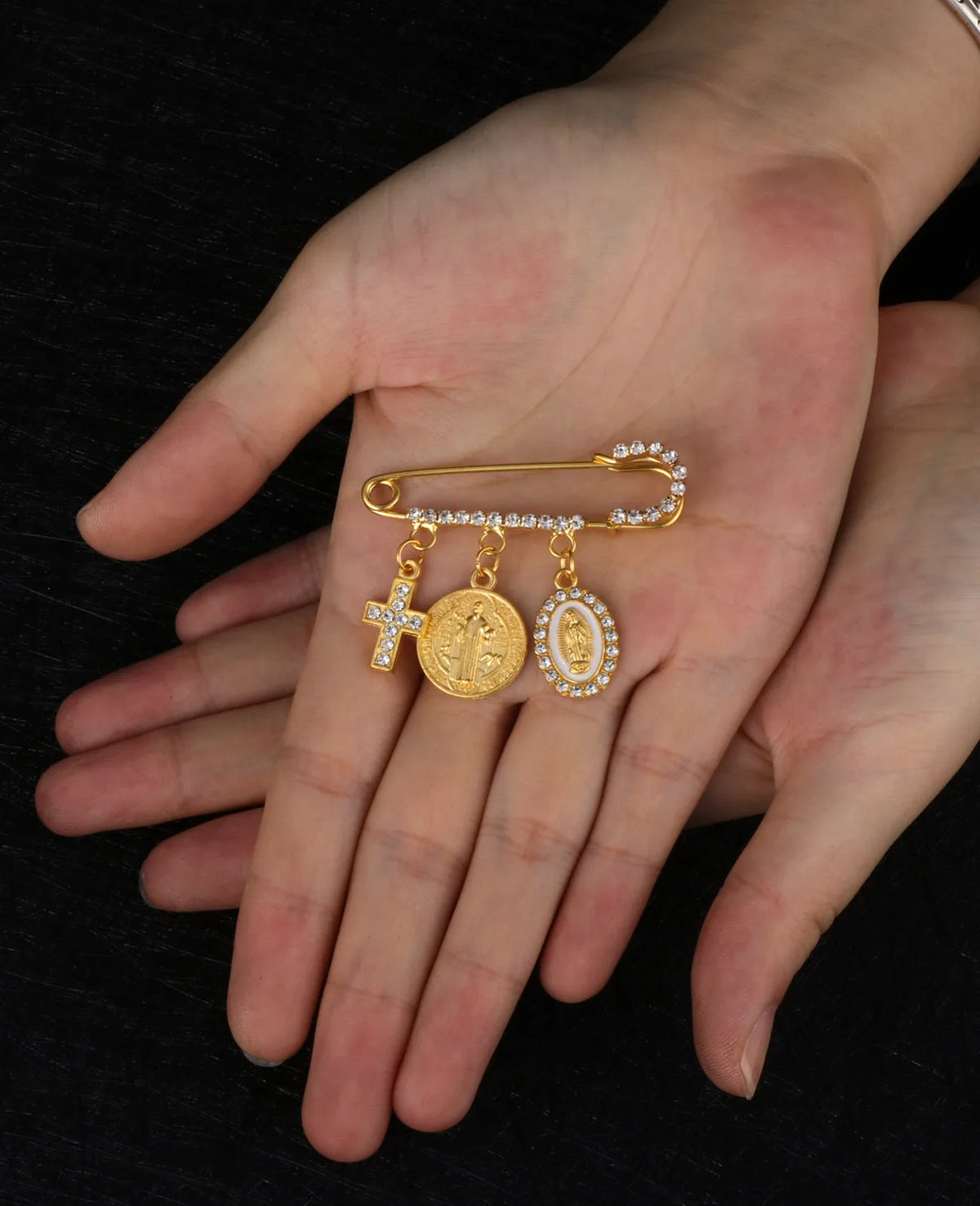 Eine Hand hält eine goldfarbene St. Benedikt-Medaille-Spange mit drei kleinen Medaillons und funkelnden Steinen.