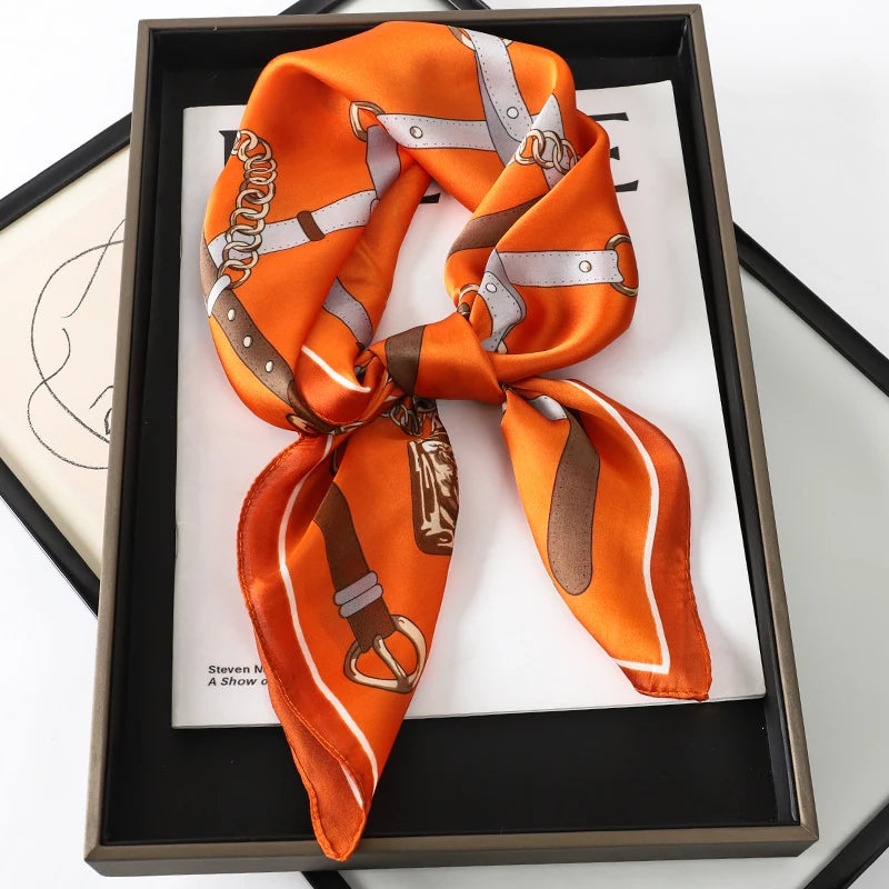 An orange silk scarf tied in a knot with silver and brown accents displayed in a black box.