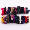 A colorful set of velvet scrunchies in various shades of purple, pink, green, and blue hair ties.