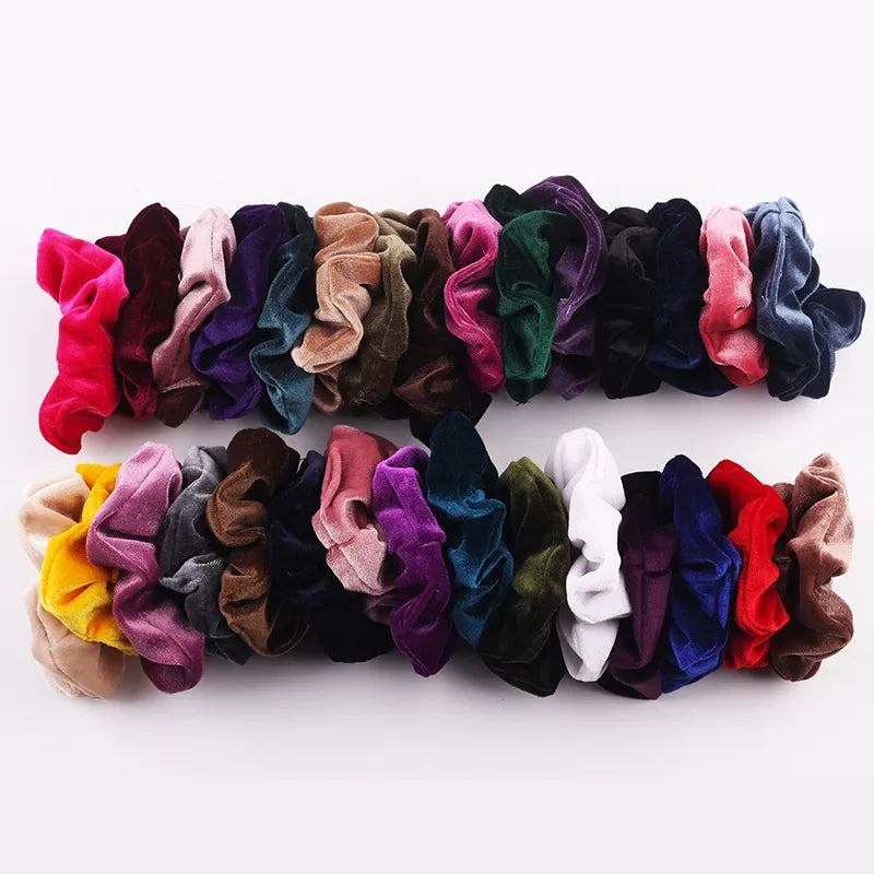 A colorful set of velvet scrunchies in various shades of purple, pink, green, and blue hair ties.
