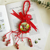 A red ribbon tied into a bow holds a wooden cross pendant with a green and gold design.