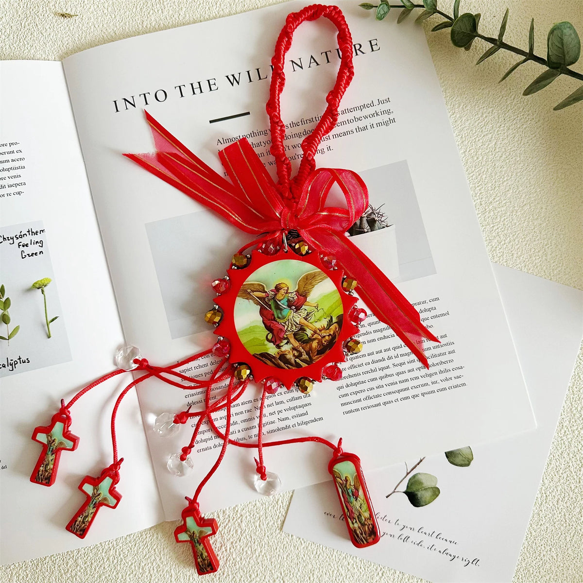 A red ribbon tied into a bow holds a wooden cross pendant with a green and gold design.