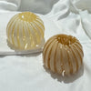 A close-up of elegant horsetail hair clips in a pale yellow color arranged on a white plate.